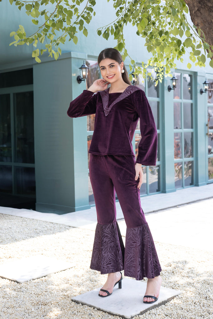 A woman wearing a full sleeve, relaxed fit, Velvet Co-Ord set with V-neck and metallic print at the bottom in purple color 
