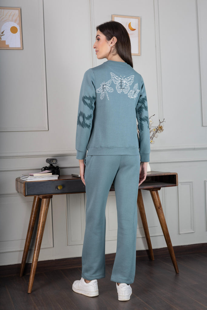 A woman wearing a full sleeve, relaxed fit, fleece co ord set with round neck and back prints in sea green Color 